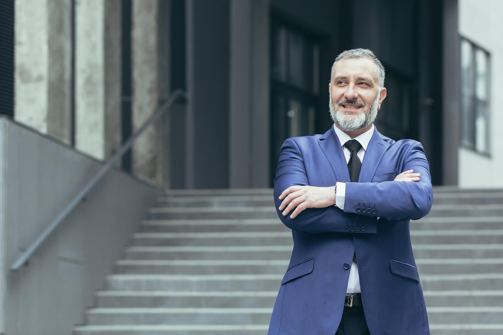Home portrait of senior real estate agent man. he stands next to a business suit near a modern building
